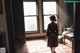 A woman in a brown robe standing in front of a window.