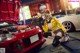 A woman kneeling down next to a red car in a garage.